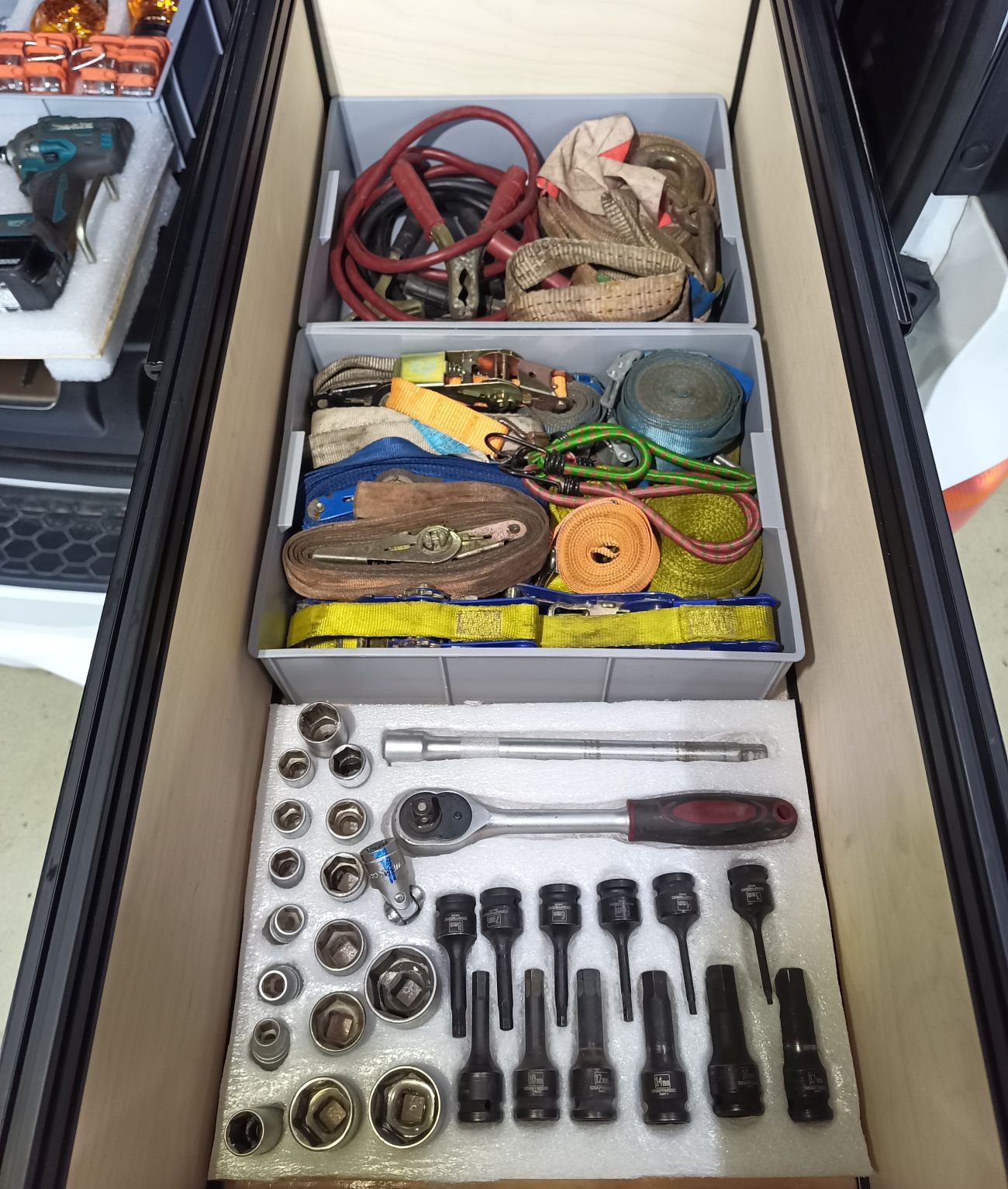Open drawer with various tools and equipment including a set of sockets and wrenches.