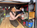 pulling out clear bin off of shelving inside van that has been converted for camping with a diy kit from TNTvans